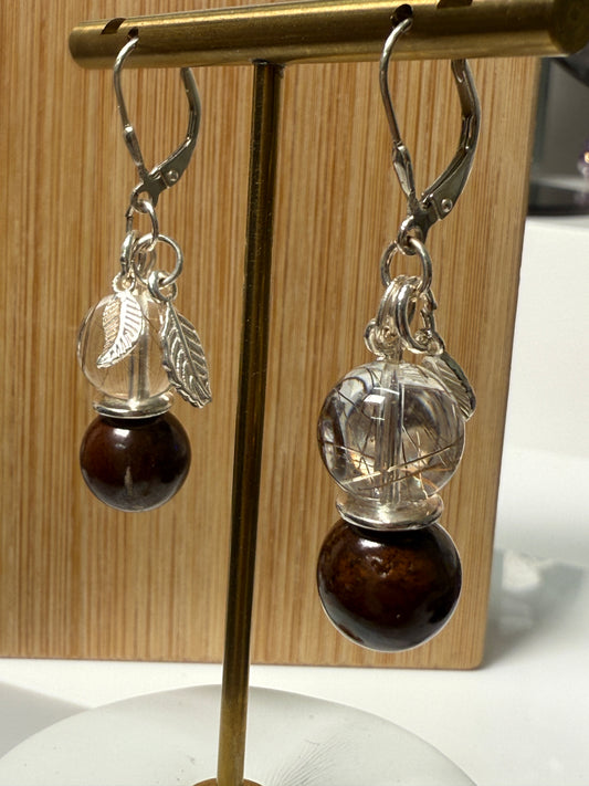 Close-up of a pair of crystal earrings featuring Rutile-in-Quartz and Brown Opal stones, accented with silver leaf charms. Displayed against a soft neutral background.