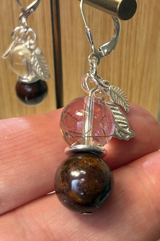Close-up of a pair of crystal earrings featuring Rutile-in-Quartz and Brown Opal stones, accented with silver leaf charms. Displayed against a soft neutral background.