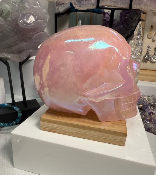 Large Pink Aura Rose Quartz crystal skull, measuring approximately 5 x 5.5 inches and weighing 4 lbs. Features soft pink coloration and a glowing, iridescent surface. Displayed as a carved decorative stone with heart-focused elegance.