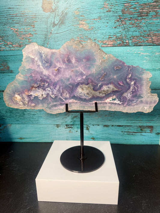 Pink, purple, and blue Fluorite crystal slab on a modern black stand, used as elegant home decor